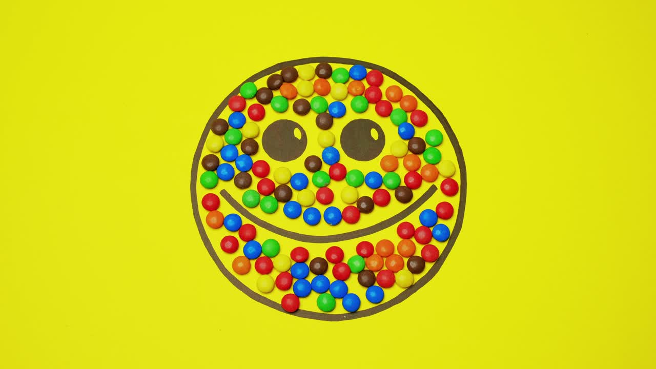 sonriente en fondo amarillo lleno de dulces de colores. los dulces redondos se alejan de la imagen.