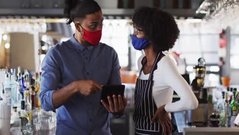 Diversos-Trabajadores-De-Cafeterías,-Hombres-Y-Mujeres,-Que-Usan-Máscaras-Faciales-En-Una-Cafetería-Usando-Una-Tableta-Digital-Hablando