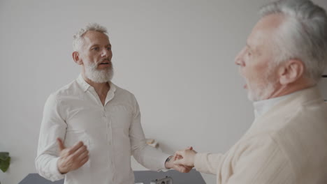 two happy senior men friends greeting each other with a hug and laughing at home