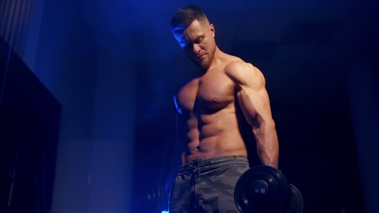 Giovane uomo che tiene un manubrio. Atleta in forma che allena i bicipiti in palestra.