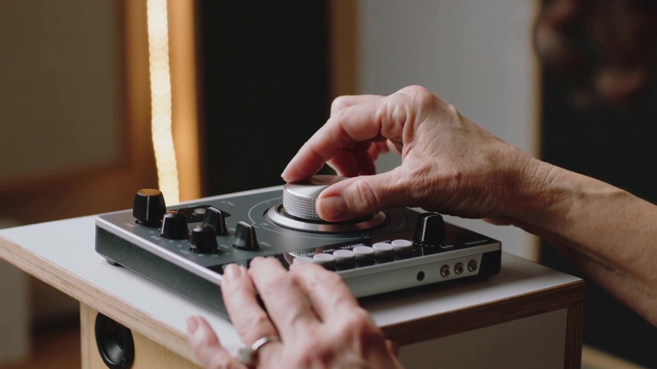 La mano destra di un anziano che regola una rotella jog per ottimizzare l'audio in uno studio domestico, premendo i pad.