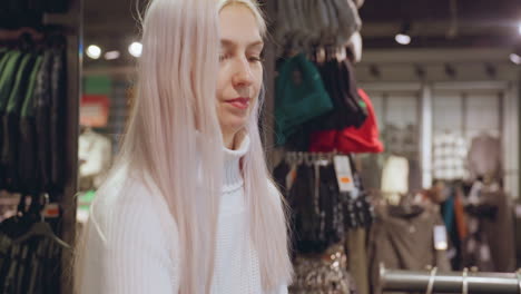 shopping mom with platinum hair in white turtleneck inspects shearling winter coat, fingertips testing plush lining, checks price tag under warm boutique lighting, then returns garment to rack