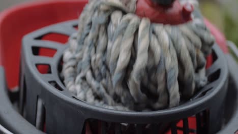 wringing cleaning mop into red bucket close up