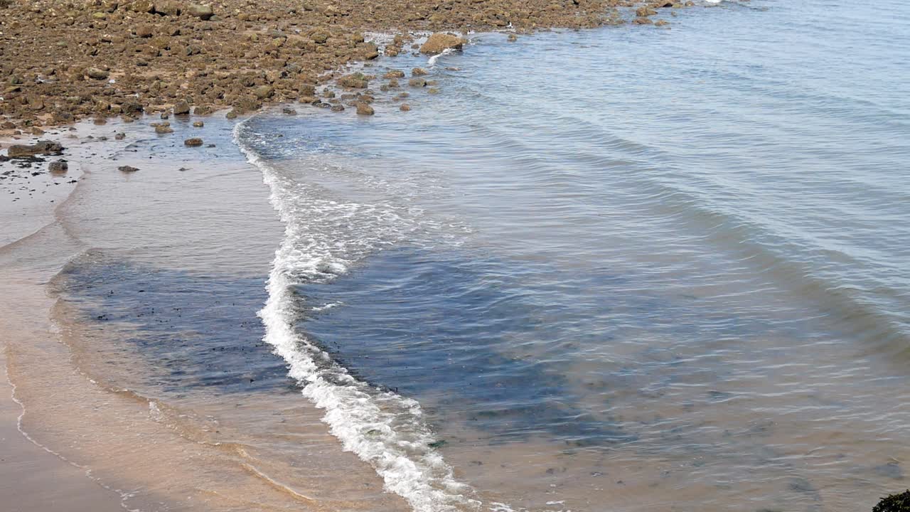 Onde di marea chiare e soleggiate si infrangono contro la riva ghiaiosa.
