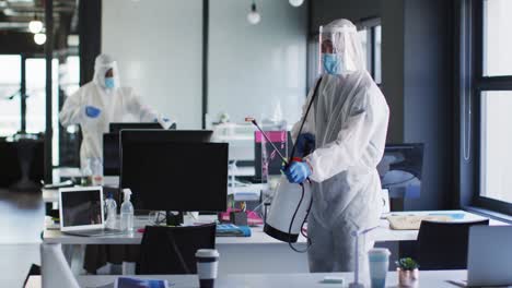 trabajador de la salud con ropa de protección limpiando la oficina con un pulverizador de desinfectante