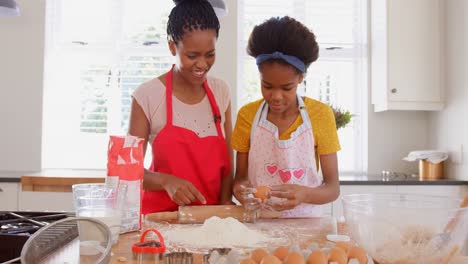 Front-view-of-young-black-daughter-cracking-egg-on-flour-in-kitchen-of-comfortable-home-4k