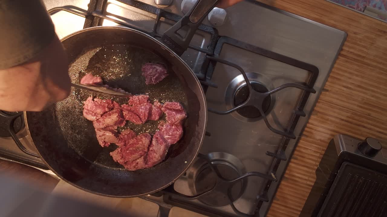 Domestic cook stirring mince beef in hot frying pan TOP DOWN view