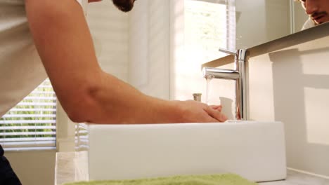 Man-washing-his-face-with-water-in-bathroom