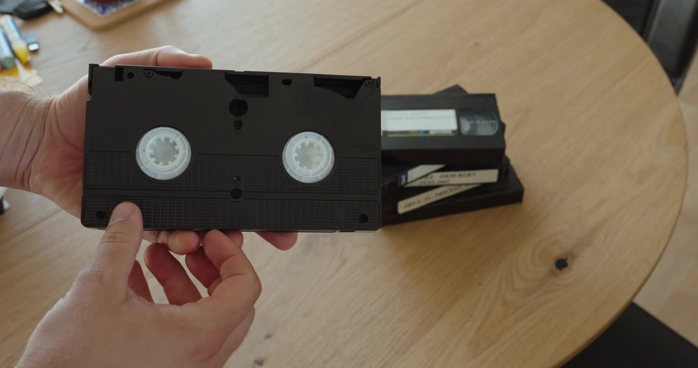 Close-up of hands inspecting an old VHS cassette tape and checking its condition. Ideal for vintage technology, video archives, media preservation, data storage, and digitization concepts.