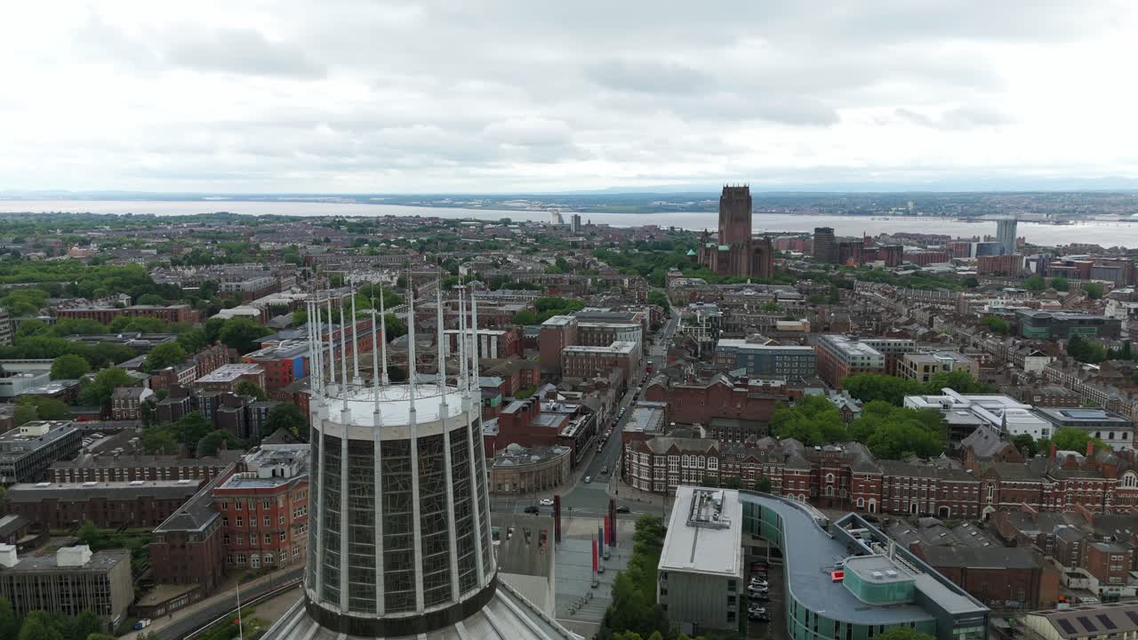 Aerial view of Liverpool Metropolitan Cathedral and surrounding cityscape, with River Mersey and Anglican Cathedral visible in the distance on a cloudy day