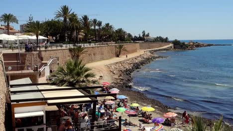 punta prima, spain - : yacht goes by and people on beach enjoying the sun on the costa blanca coastline