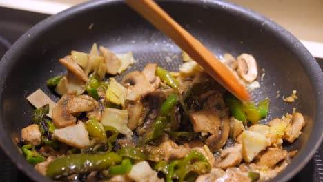 close up view of stir fry vegetables with wooden tea spoon consisting of pepper, mushroom, garlic and rosemary in the kitchen