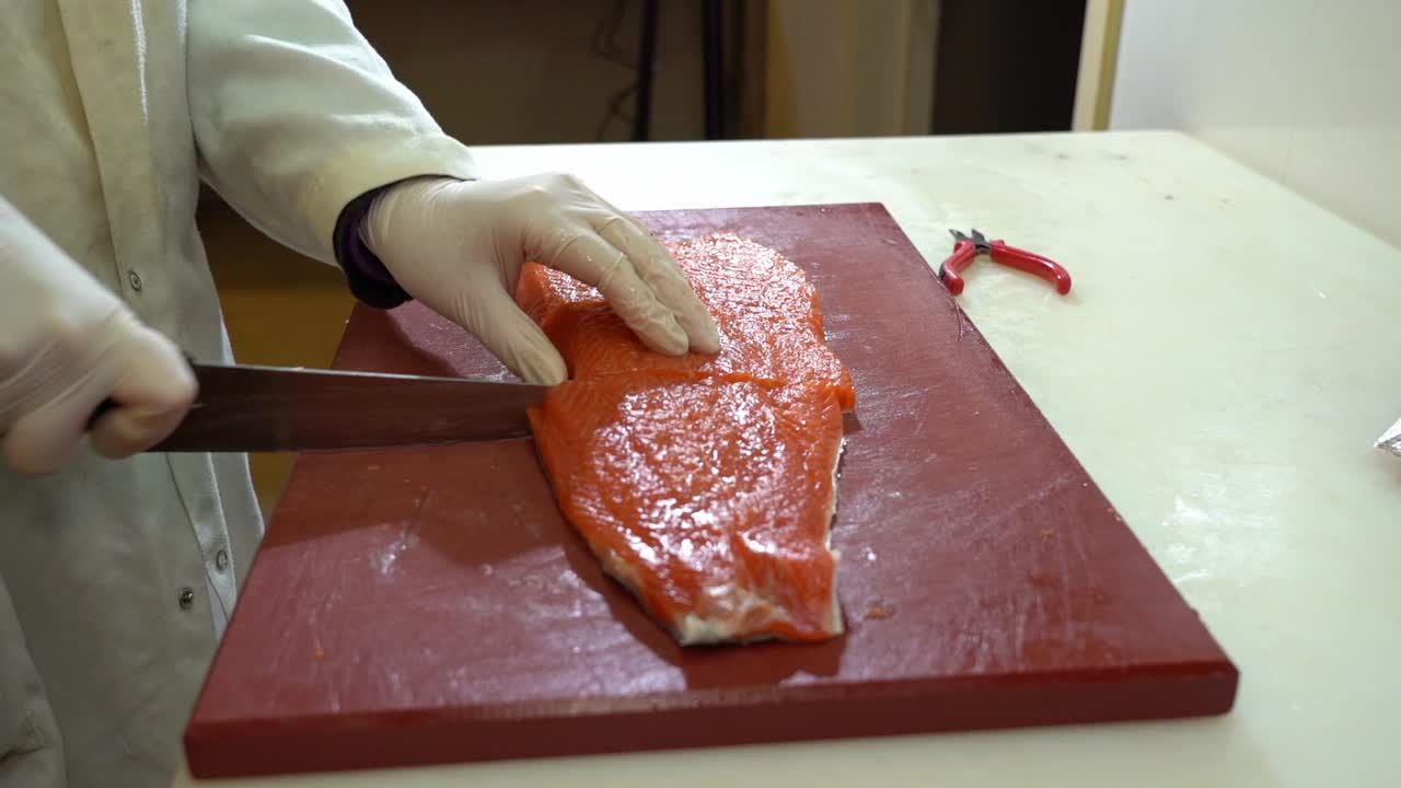 White coated fish industry worker cutting a salmon filet in two pieces - slow motion static shot from the side