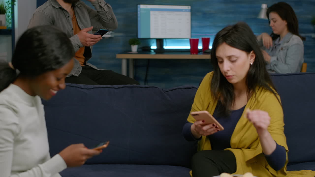 다인종 친구 들 이 소파 에 앉아서 별도로 전화 를 하고 인터넷 을 서핑 하고 있다