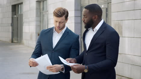 Businessmen-discussing-documents-on-street.Employees-standing-on-street-together