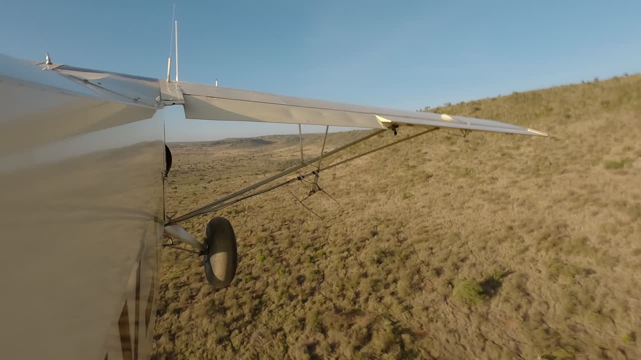 Kleines Flugzeug in Seitenansicht fliegt tief über Sträuchern und Hügeln