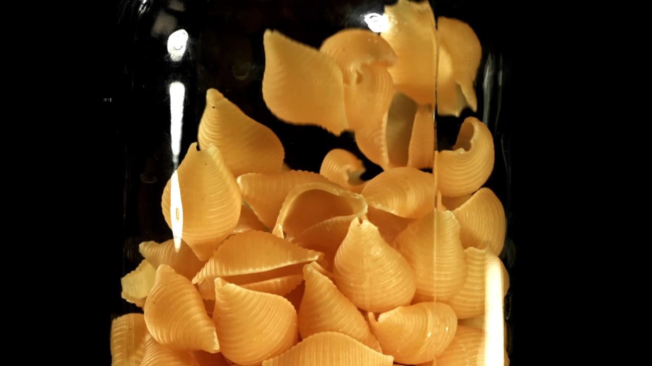 Uncooked Conchiglie Pasta Falling into a Glass Jar