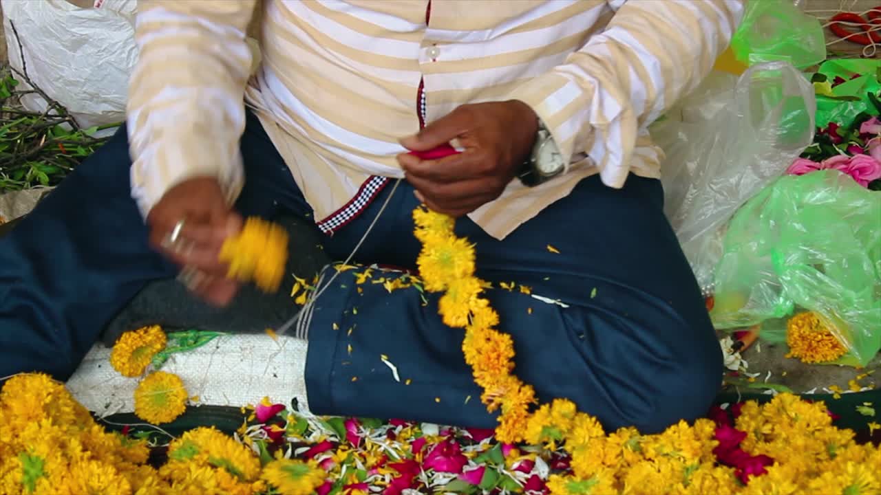 Primo piano di un uomo che realizza una ghirlanda di fiori di calendula per tempio, matrimonio o festival. Tradizione indiana e lavoro artigianale. Ottimo per video su cultura, rituali o artigianato