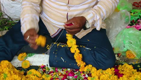 close-up of man making marigold flower garland for temple, wedding or festival. indian tradition and handmade work. great for culture, rituals or craft videos.