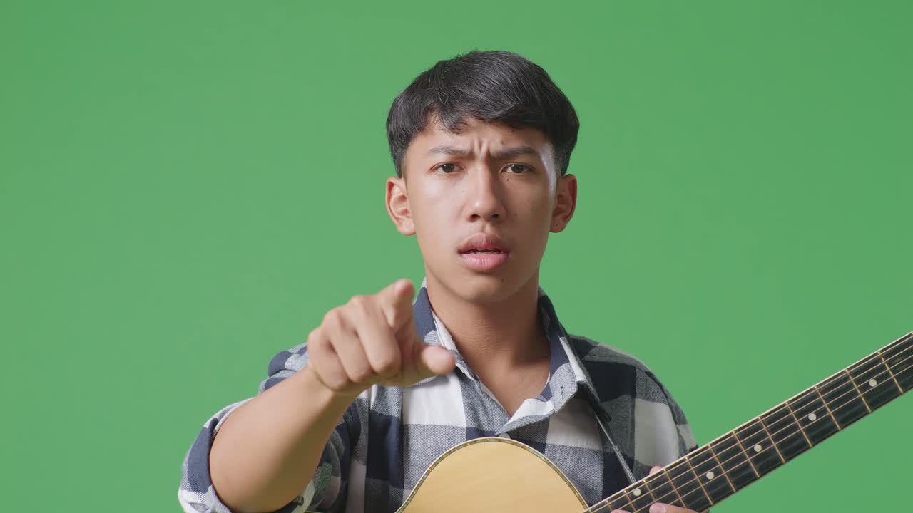 녹색 스크린 배경에 서 있는 동안 기타를 들고 카메라에 소리치는 아시아 십대