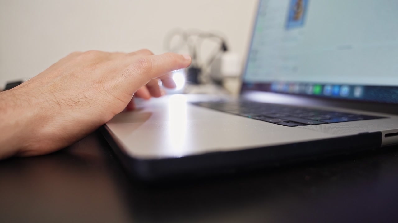 Close-up of a man's hand using a laptop trackpad to browse the internet on a desk in a modern office. Cinematic shallow depth of field shot for corporate lifestyle and business ads.