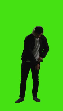 Vertical-Video-Full-Length-Shot-Of-Man-Wearing-Wireless-Headphones-Streaming-Music-From-Mobile-Phone-Against-Green-Screen