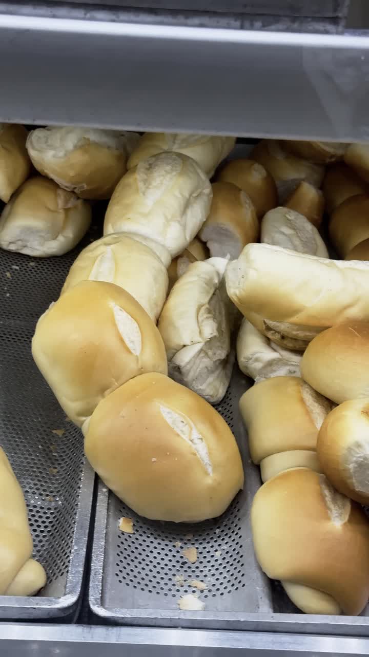 4K vertical close-up of freshly baked Brazilian French bread, known as pão de sal, in a bakery. The golden crust and fluffy texture highlight the artisanal quality, perfect for culinary visuals.