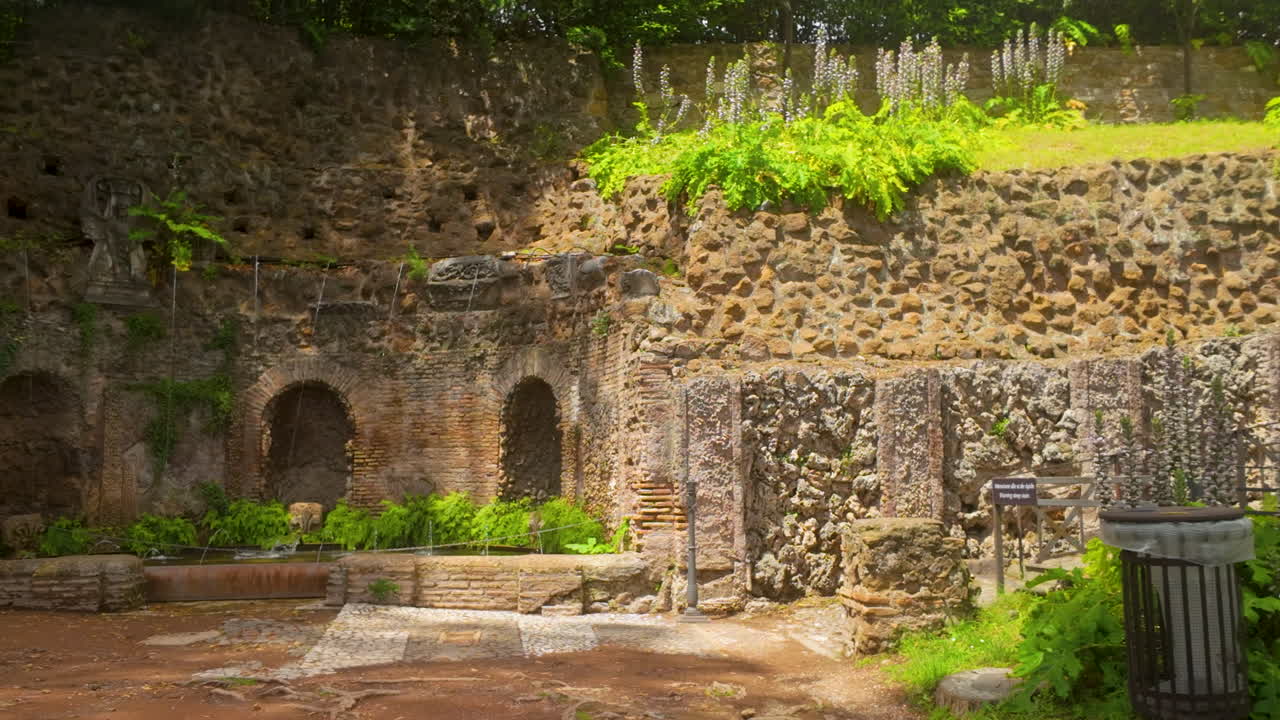 Ancient Roman fountain ruins covered in greenery, water trickling from arched wall niches