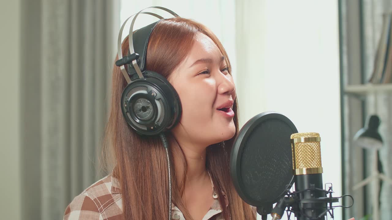 Young Asian Woman In Headphones Singing Into Microphone During Online Livestream In Podcast Studio