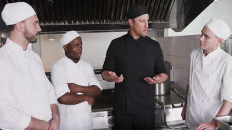 diverse male chef instructing group of trainee male chefs in kitchen, slow motion