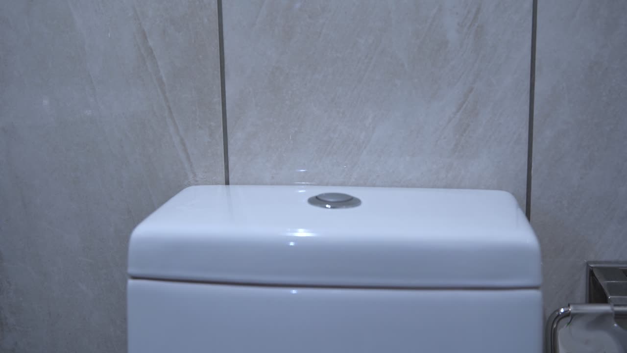 Close-up of hand pressing flush button on modern toilet. Great for hygiene, sanitation, or bathroom product use.