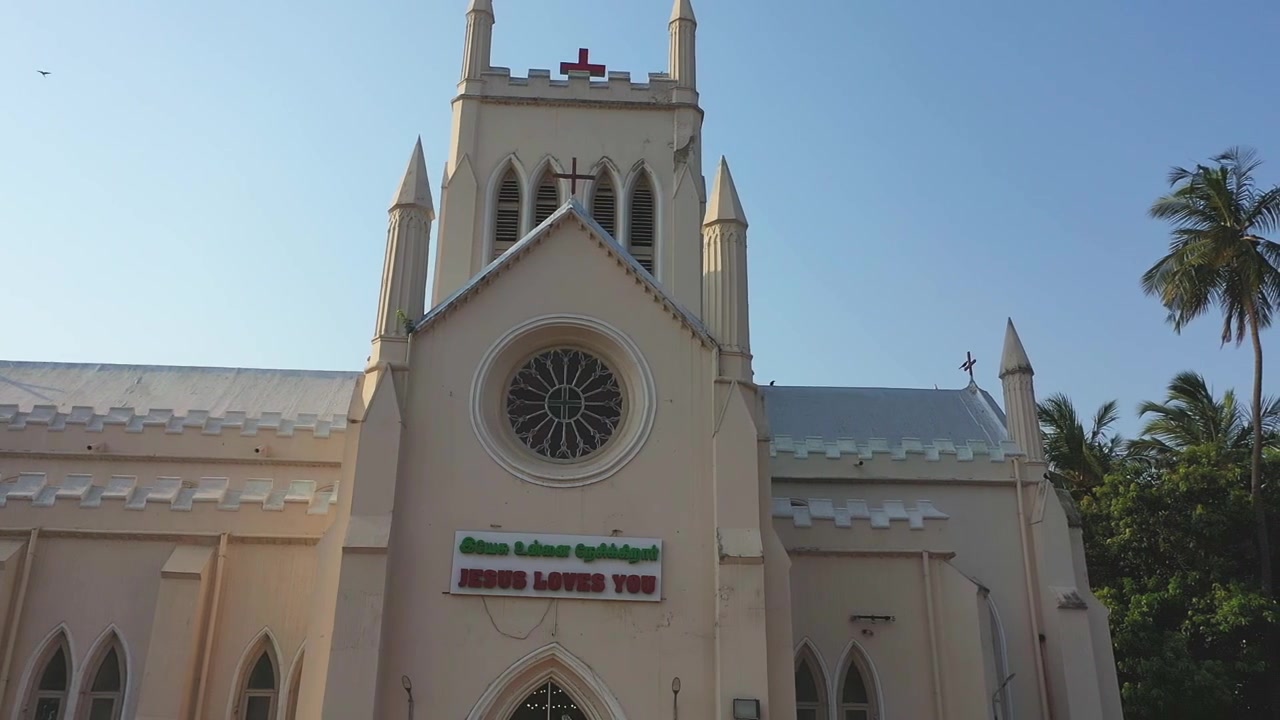 Tomada panorâmica em ângulo baixo da Igreja do Sul da Índia, exibindo arquitetura gótica, torre sineira e fachada branca sob céu azul claro durante o dia em Chennai, Tamil Nadu, Índia.