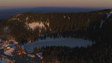 flyover shot over the frozen black forest lake called mummelsee at sunset in winter