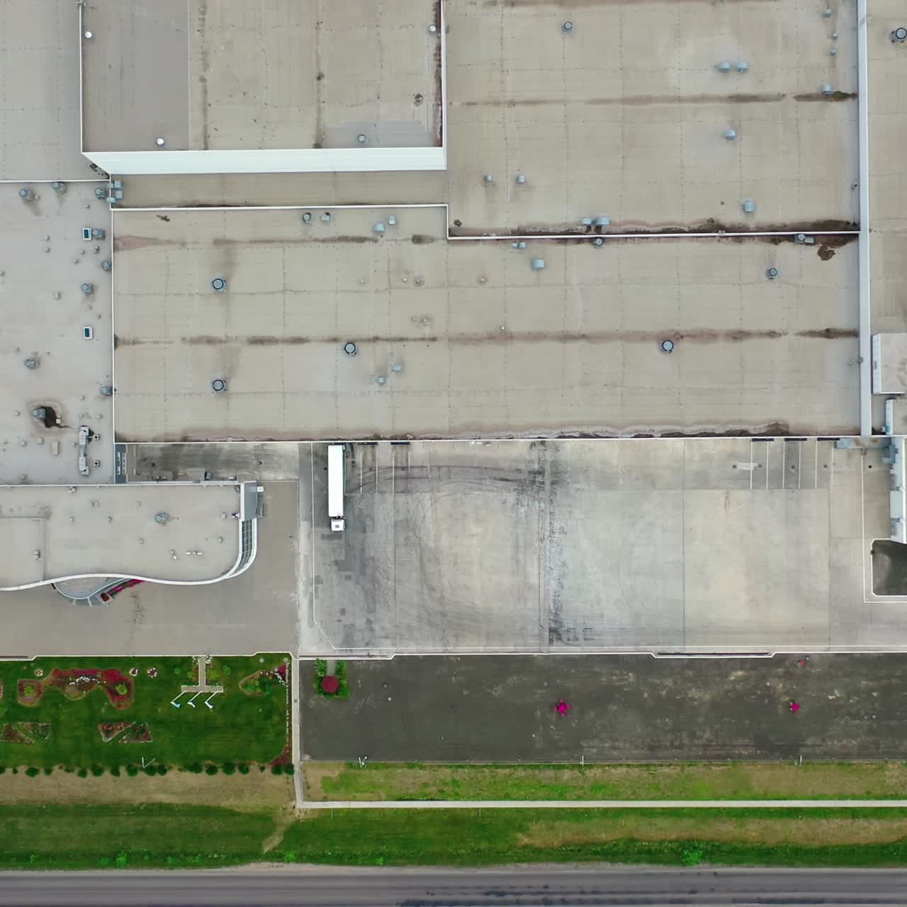 Grey roof of a large plant. Exterior of a factory with parking spaces. industry on field. Camera rising. Top view