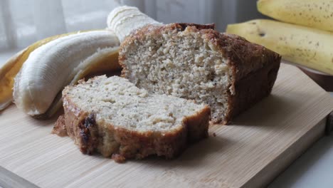 freshly baked banana bread on a wooden cutting board with ripe bananas in the background