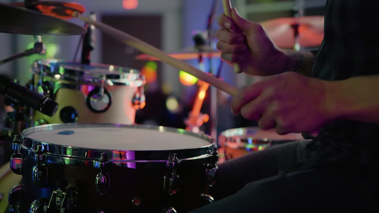 primo piano uomo caucasico sul palco illuminato con bacchette che suonano la batteria