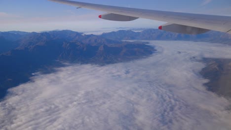 aerial view of mountains and flying above clouds with view of airplane wing