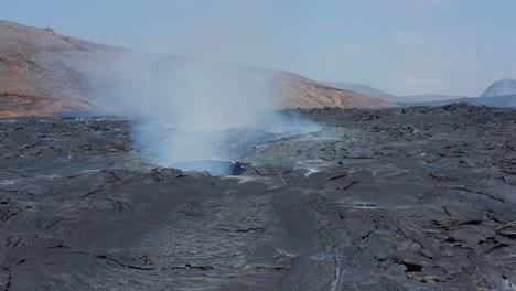 Slide-and-pan-footage-of-smoke-coming-out-from-hole-in-layer-of-cooling-lava-in-new-lava-field.--Fagradalsfjall-volcano.-Iceland,-2021