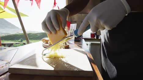 sección media de hombre afroamericano con guantes rallando queso en el camión de comida