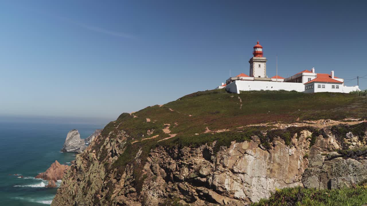 Static shot of Cabo da Roca lighthouse perched on a dramatic cliff above the Atlantic Ocean under a clear sky
