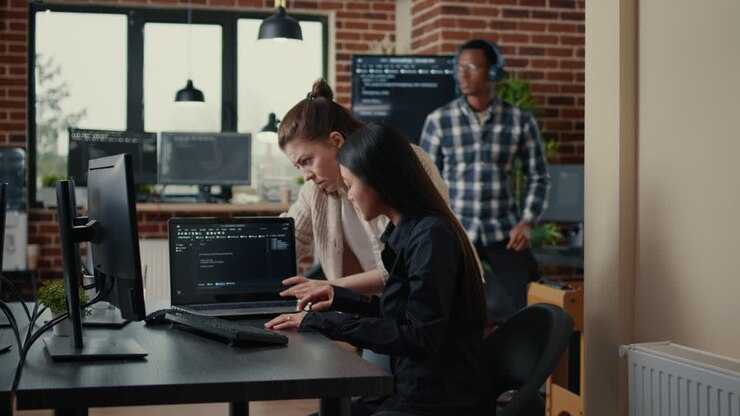 Team of software developers comparing source codes running on laptop screen and computer monitor