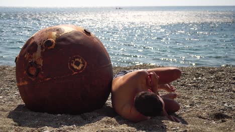 hombre haciendo ejercicio de yoga al aire libre cerca de una vieja mina marina flotante oxidada en la playa con costa rocosa y fondo marino. estilo de vida saludable, contaminación, protección de la naturaleza, concepto de guerra y paz