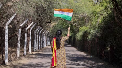 young girl waving the indian tricolor national flag at remote location at day from back angle