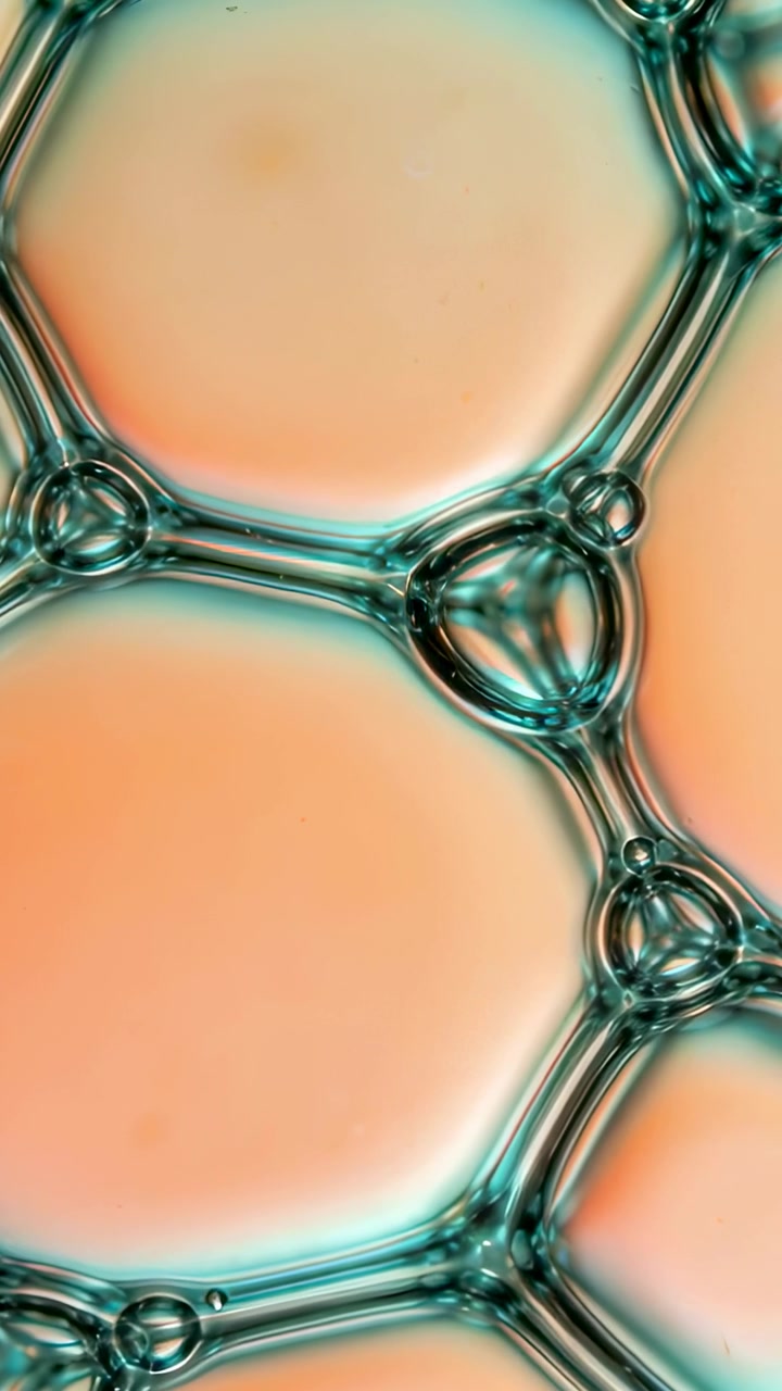 Video verticale: Esagoni di pellicola di sapone che si spostano, formando goccioline con luce color pesca, in macro.