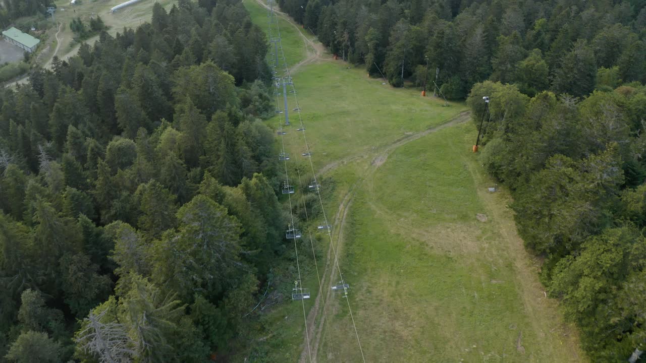 вид с воздуха на пролетающую над курортом канатную дорогу среди деревьев дикого леса