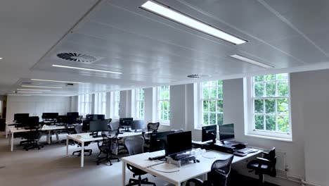 a well-lit spacious open plan empty office with modern workstations, ergonomic chairs, and large windows