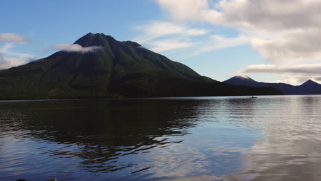 as the sun ascends a serene glassy lake reflects its golden hues, framed by lush, majestic mountains in tranquil morning glory