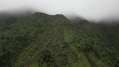 aerial flies down steep ridge trail to hiker in mountain fog on hawaii