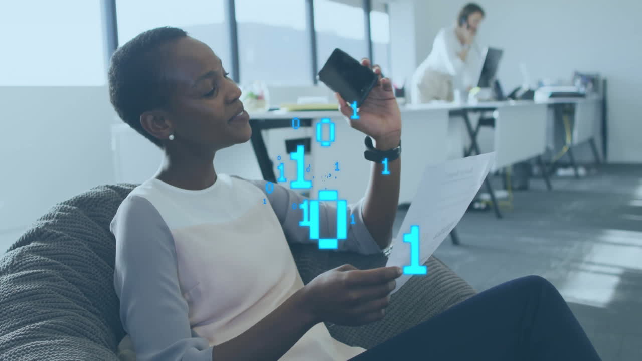 Animation of binary data processing over african american woman talking on phone in casual office