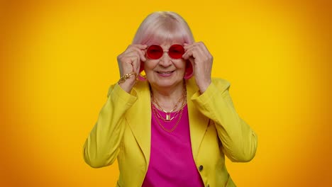 feliz juguetona anciana abuela mujer con gafas de sol rojas parpadeando el ojo, mirando a la cámara con una sonrisa